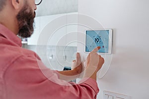 Man using smart thermostat, adjusting, lowering heating temperature at home. Concept of sustainable, efficient, and