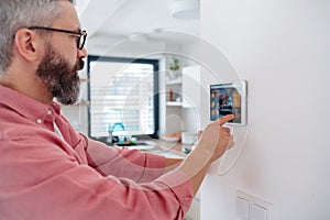 Man using smart thermostat, adjusting, lowering heating temperature at home. Concept of sustainable, efficient, and
