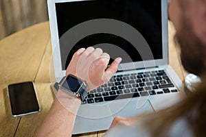 Man using smart watch with laptop and mobile phone on table in cafe