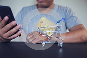 Man using smartphone with credit card in small shopping cart.