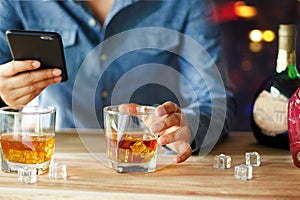 Man using smartphone while drinking whiskey alcohol beverage a