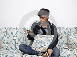 Man is using a smartphone for the internet while relaxed sitting on the sofa at his modern home