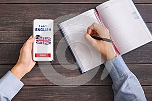 Man using smartphone with Learning English app and writing notes
