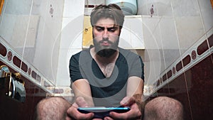 Man using a smartphone while sitting on toilet. He is typing a message.