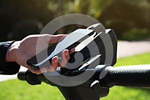 Man using smartphone to pay and unblock rental electric scooter outdoors, closeup photo