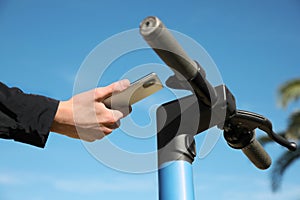 Man using smartphone to pay and unblock rental electric scooter outdoors, closeup photo