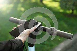 Man using smartphone to pay and unblock rental electric scooter outdoors, closeup photo