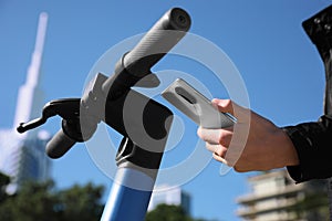 Man using smartphone to pay and unblock rental electric scooter outdoors, closeup photo