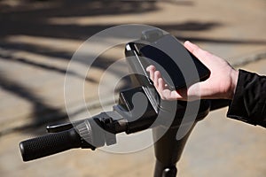 Man using smartphone to pay and unblock rental electric scooter outdoors, closeup photo