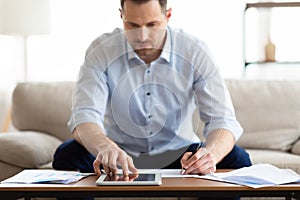 Man using tablet at home and writing notes