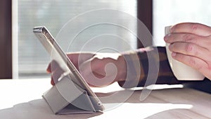 Man using tablet. Person drinking morning coffee and checking internet.