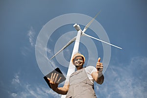 Man using tablet and and showing thumb up near wind turbines