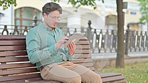 Man using Tablet while Sitting on Park Bench