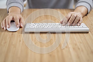 Man using white computer keyboard and mouse on the wooden desk