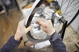 Man using a wrench to tighten the spokes of a bicycle wheel in his bike workshop