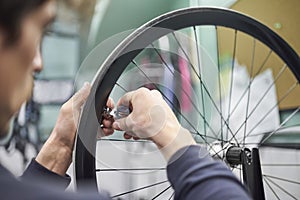 Man using a wrench to tighten the spokes of a bicycle wheel in his bike workshop