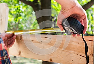 Man using yellow measuring tape to measure length of wooden board