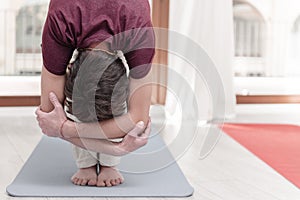 Man in uttanasana with elbow grab. Intense stretch pose, forward bend, head to knees. Seguence of Surya namaskar.