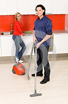 Man vacuuming, woman in background