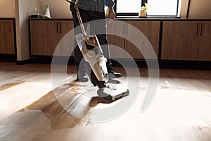 Man vacuuming wooden floor in loft iving room with vacuum cleaner. Close up