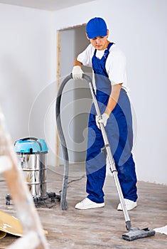 Man vacuums the floor - professional cleaning after renovation in room