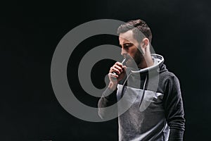 Young man vaping e-cigarette with smoke on black