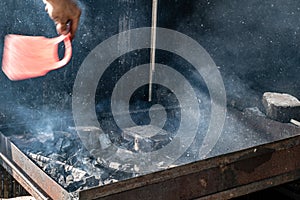 Man ventilating hot burned coals before grilling