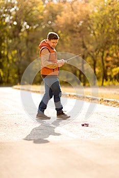 Man in vest playing with toy car on remote control in autumn Park