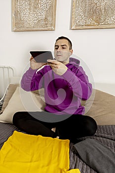 Man with violet hoodie using digital tablet, takes a photo of his old clothes to sell them online. Selling on website, e