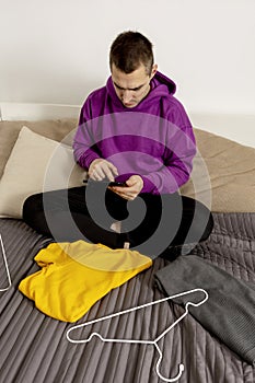 Man with violet hoodie using digital tablet, takes a photo of his old clothes to sell them online. Selling on website, e