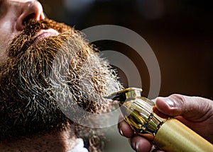 Man visiting hairstylist in barbershop. Barber works with a beard clipper. Hipster client getting haircut. Hands of a