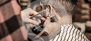 Man visiting hairstylist in barbershop. Barber works with hair clipper. Hipster client getting haircut. Hands of barber