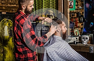 Man visiting hairstylist in barbershop. Hairdresser does styling with a comb in barbershop. Bearded man in barber shop