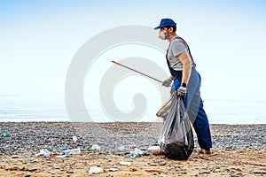 Man volunteer collecting garbage on the beach with a reach extender stick