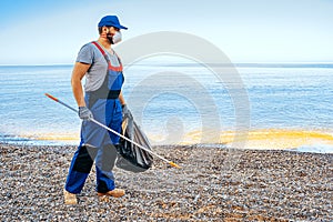 Man volunteer collecting garbage on the beach with a reach extender stick