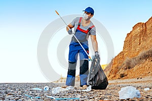 Man volunteer collecting garbage on the beach with a reach extender stick