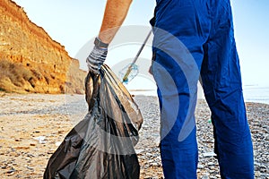 Man volunteer collecting garbage on the beach with a reach extender stick