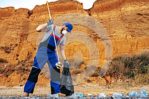 Man volunteer collecting garbage on the beach with a reach extender stick