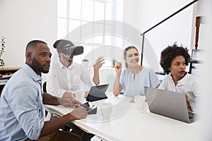 Man in VR goggles at a desk with colleagues in an office photo