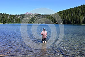 Man wading in Todd Lake, Oregon, with Broken Top in background.