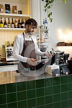 Man waiter working in coffee shop using terminal while standing at counter