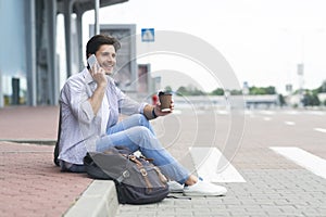 Man waiting outside of airport, drinking coffee and talking on cellphone