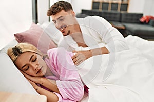 Man waking up his girlfriend lying on the bed at home
