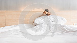 Man waking up and use smartphone or mobile phone on the bed in white blanket at morning time