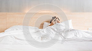 Man waking up and use smartphone or mobile phone on the bed in white blanket at morning time