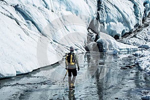 Man walking across the Matanuska Glacier below wall of white ice