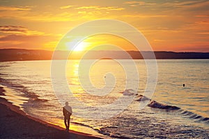 Man walking alone on the beach at sunset. Calm sea