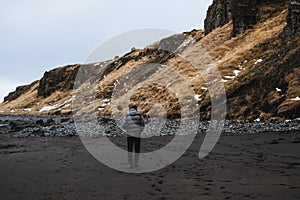 A man walking alone on black sand beach with cliff