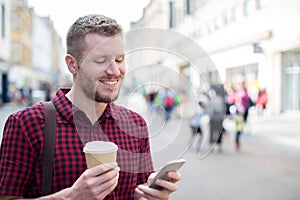 Man Walking Along City Street Reading Text Message On Mobile Phone