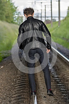 Man walking balancing on railroad tracks. Concept: dangerous walk, carelessness and recklessness, risk to life.